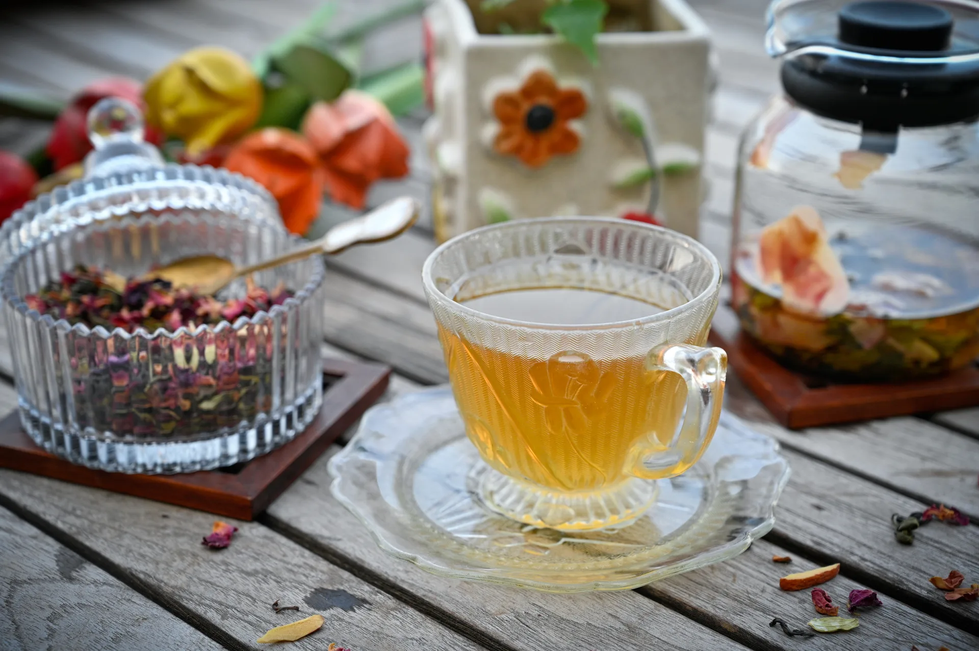 A glass cup of golden Kashmiri kahwa beside a jar of dried rose petals and spices A glass cup of golden Kashmiri kahwa beside a jar of dried rose petals and spices
